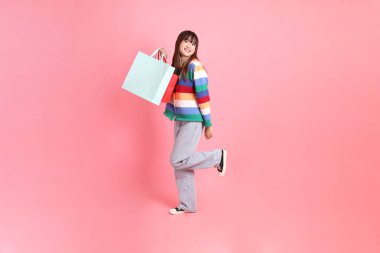 Renkli gökkuşağı kıyafetleri giyen Asyalı bir kadın ya da sıradan görünüşlü, pembe arka planda izole edilmiş alışveriş çantası taşıyan bir jest. Gen Z