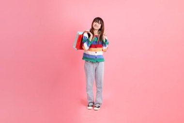 Renkli gökkuşağı kıyafetleri giyen Asyalı bir kadın ya da sıradan görünüşlü, pembe arka planda izole edilmiş alışveriş çantası taşıyan bir jest. Gen Z