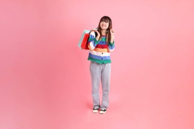 Renkli gökkuşağı kıyafetleri giyen Asyalı bir kadın ya da sıradan görünüşlü, pembe arka planda izole edilmiş alışveriş çantası taşıyan bir jest. Gen Z