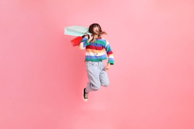 Renkli gökkuşağı kıyafetleri giyen Asyalı bir kadın ya da sıradan görünüşlü, pembe arka planda izole edilmiş alışveriş çantası taşıyan bir jest. Gen Z