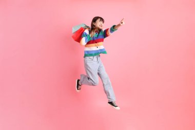 Renkli gökkuşağı kıyafetleri giyen Asyalı bir kadın ya da sıradan görünüşlü, pembe arka planda izole edilmiş alışveriş çantası taşıyan bir jest. Gen Z