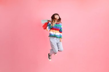 Renkli gökkuşağı kıyafetleri giyen Asyalı bir kadın ya da sıradan görünüşlü, pembe arka planda izole edilmiş alışveriş çantası taşıyan bir jest. Gen Z