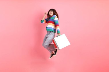 Renkli gökkuşağı kıyafetleri giyen Asyalı bir kadın ya da sıradan görünüşlü, pembe arka planda izole edilmiş alışveriş çantası taşıyan bir jest. Gen Z