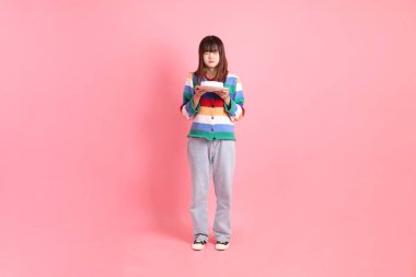 Renkli gökkuşağı kış kıyafetleri giyen Asyalı bir kadın ya da pembe arka planda saklanmış doğum günü pastası tutan bir jestle sıradan bir görünüm. Gen Z