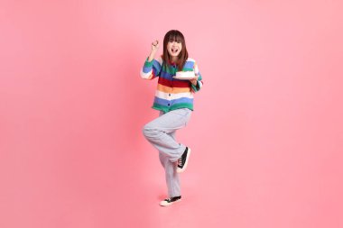 Renkli gökkuşağı kış kıyafetleri giyen Asyalı bir kadın ya da pembe arka planda saklanmış doğum günü pastası tutan bir jestle sıradan bir görünüm. Gen Z