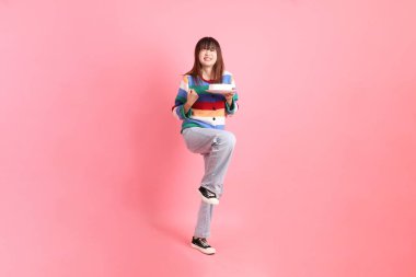 Renkli gökkuşağı kış kıyafetleri giyen Asyalı bir kadın ya da pembe arka planda saklanmış doğum günü pastası tutan bir jestle sıradan bir görünüm. Gen Z