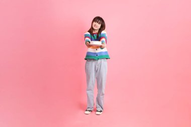 Renkli gökkuşağı kış kıyafetleri giyen Asyalı bir kadın ya da pembe arka planda saklanmış doğum günü pastası tutan bir jestle sıradan bir görünüm. Gen Z