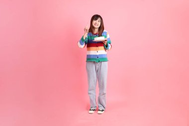 Renkli gökkuşağı kış kıyafetleri giyen Asyalı bir kadın ya da pembe arka planda saklanmış doğum günü pastası tutan bir jestle sıradan bir görünüm. Gen Z