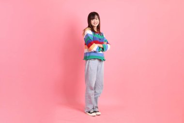 Renkli gökkuşağı kıyafetleri giyen Asyalı bir kadın ya da pembe arka planda duran ve gülümseyen bir jestle sıradan görünen bir kadın. Gen Z