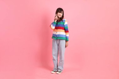 Renkli gökkuşağı kıyafetleri giyen Asyalı bir kadın ya da barış işareti olan sıradan bir görünüş, pembe arka planda iki parmak izole edilmiş V işareti. Gen Z