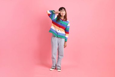 Renkli gökkuşağı kıyafetleri giyen Asyalı bir kadın ya da barış işareti olan sıradan bir görünüş, pembe arka planda iki parmak izole edilmiş V işareti. Gen Z