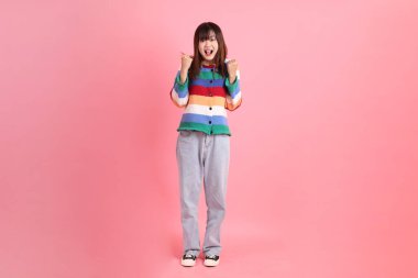 Renkli gökkuşağı kıyafetleri giyen Asyalı bir kadın ya da pembe arka planda izole edilmiş, heyecanlı ve kutlama yapan bir jest. Gen Z