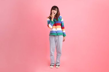 Renkli gökkuşağı kıyafetleri giyen Asyalı bir kadın ya da sürpriz jestli sıradan bir görünüş ve pembe arka planda etkileyici bir izolasyon. Gen Z