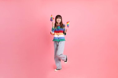 Renkli gökkuşağı kıyafetleri giyen Asyalı bir kadın ya da pembe arka planda Gurur Bayraklarını Tutma jesti olan sıradan görünüşlü bir kadın. Gen Z