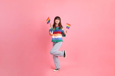 Renkli gökkuşağı kıyafetleri giyen Asyalı bir kadın ya da pembe arka planda Gurur Bayraklarını Tutma jesti olan sıradan görünüşlü bir kadın. Gen Z