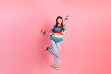 Renkli gökkuşağı kıyafetleri giyen Asyalı bir kadın ya da pembe arka planda Gurur Bayraklarını Tutma jesti olan sıradan görünüşlü bir kadın. Gen Z