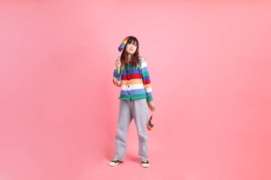 Renkli gökkuşağı kıyafetleri giyen Asyalı bir kadın ya da pembe arka planda Gurur Bayraklarını Tutma jesti olan sıradan görünüşlü bir kadın. Gen Z