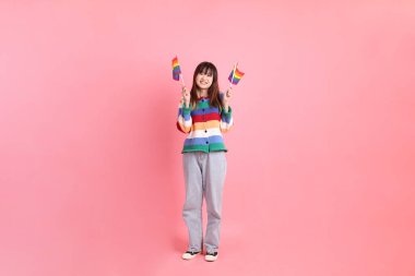 Renkli gökkuşağı kıyafetleri giyen Asyalı bir kadın ya da pembe arka planda Gurur Bayraklarını Tutma jesti olan sıradan görünüşlü bir kadın. Gen Z