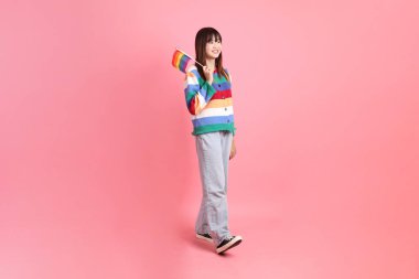 Renkli gökkuşağı kıyafetleri giyen Asyalı bir kadın ya da pembe arka planda Gurur Bayraklarını Tutma jesti olan sıradan görünüşlü bir kadın. Gen Z