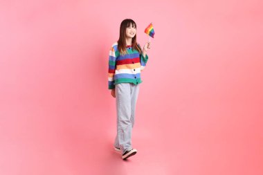 Renkli gökkuşağı kıyafetleri giyen Asyalı bir kadın ya da pembe arka planda Gurur Bayraklarını Tutma jesti olan sıradan görünüşlü bir kadın. Gen Z