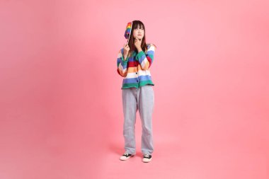 Renkli gökkuşağı kıyafetleri giyen Asyalı bir kadın ya da pembe arka planda izole edilmiş olarak düşünürken Onur Bayraklarını Tutma jesti ile sıradan görünen bir kadın. Gen Z