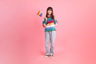 Renkli gökkuşağı kıyafetleri giyen Asyalı bir kadın ya da pembe arka planda Gurur Bayraklarını Tutma jesti olan sıradan görünüşlü bir kadın. Gen Z