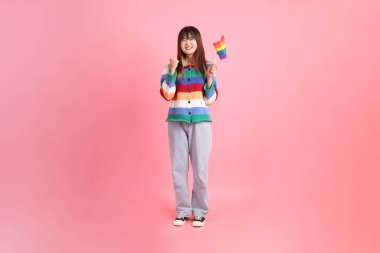 Renkli gökkuşağı kıyafetleri giyen Asyalı bir kadın ya da pembe arka planda Gurur Bayraklarını Tutma jesti olan sıradan görünüşlü bir kadın. Gen Z