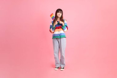 Renkli gökkuşağı kıyafetleri giyen Asyalı bir kadın ya da pembe arka planda Gurur Bayraklarını Tutma jesti olan sıradan görünüşlü bir kadın. Gen Z