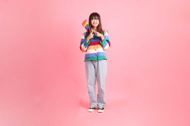 Renkli gökkuşağı kıyafetleri giyen Asyalı bir kadın ya da pembe arka planda Gurur Bayraklarını Tutma jesti olan sıradan görünüşlü bir kadın. Gen Z