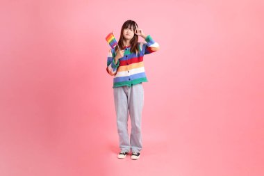 Renkli gökkuşağı kıyafetleri giyen Asyalı bir kadın ya da pembe arka planda izole edilmiş olarak düşünürken Onur Bayraklarını Tutma jesti ile sıradan görünen bir kadın. Gen Z