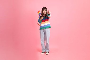 Renkli gökkuşağı kıyafetleri giyen Asyalı bir kadın ya da pembe arka planda izole edilmiş Onur Bayraklarını Tutma jesti ile gelişigüzel görünen bir kadın. Gen Z