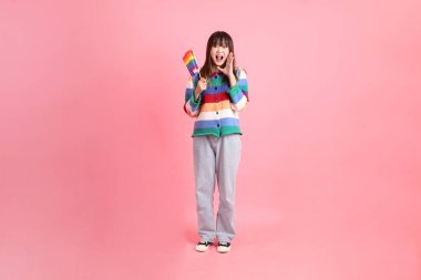 Renkli gökkuşağı kıyafetleri giyen Asyalı bir kadın ya da pembe arka planda Gurur Bayraklarını Tutma jesti olan sıradan görünüşlü bir kadın. Gen Z