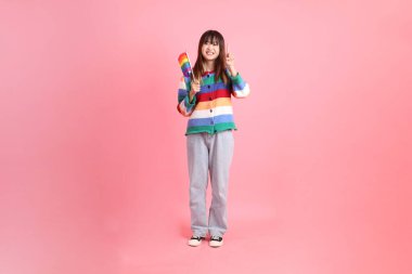 Renkli gökkuşağı kıyafetleri giyen Asyalı bir kadın ya da pembe arka planda izole edilmiş Onur Bayraklarını Tutma jesti ile gelişigüzel görünen bir kadın. Gen Z