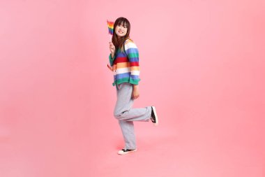 Renkli gökkuşağı kıyafetleri giyen Asyalı bir kadın ya da pembe arka planda Gurur Bayraklarını Tutma jesti olan sıradan görünüşlü bir kadın. Gen Z