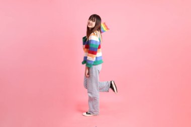 Renkli gökkuşağı kıyafetleri giyen Asyalı bir kadın ya da pembe arka planda Gurur Bayraklarını Tutma jesti olan sıradan görünüşlü bir kadın. Gen Z