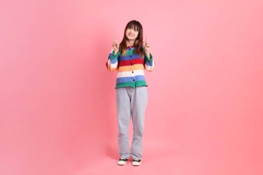 Renkli gökkuşağı kıyafetleri giyen Asyalı bir kadın ya da pembe arka planda izole edilmiş bir yeri işaret eden hareketli sıradan bir görünüm. Gen Z