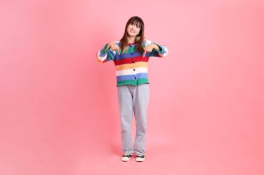 Renkli gökkuşağı kıyafetleri giyen Asyalı bir kadın ya da pembe arka planda izole edilmiş bir yeri işaret eden hareketli sıradan bir görünüm. Gen Z