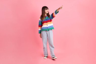 Renkli gökkuşağı kıyafetleri giyen Asyalı bir kadın ya da pembe arka planda izole edilmiş bir yeri işaret eden hareketli sıradan bir görünüm. Gen Z