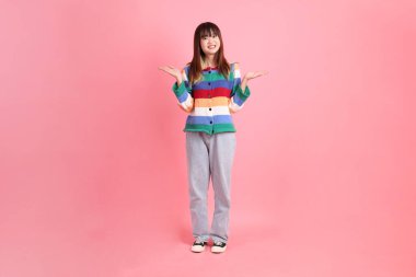 Renkli gökkuşağı kıyafetleri giyen Asyalı bir kadın ya da pembe arka planda izole edilmiş bir yeri işaret eden hareketli sıradan bir görünüm. Gen Z