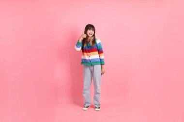 Renkli gökkuşağı kışı kıyafetleri giyen Asyalı bir kadın ya da pembe arka planda soyutlanmış bir jest yapan sıradan görünüşlü bir kadın. Gen Z