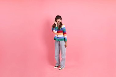 Renkli gökkuşağı kışı kıyafetleri giyen Asyalı bir kadın ya da pembe arka planda soyutlanmış bir jest yapan sıradan görünüşlü bir kadın. Gen Z