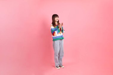 Renkli gökkuşağı kış kıyafetleri giyen Asyalı kadın ya da pembe arka planda el çırpma hareketi yapan sıradan görünüşlü. Gen Z