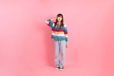 Renkli gökkuşağı kış kıyafetleri giyen Asyalı kadın ya da pembe arka planda soyutlanmış düşünme jesti ile sıradan bir görünüm. Gen Z