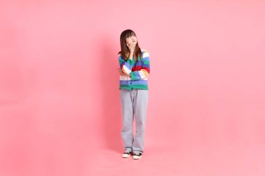 Renkli gökkuşağı kış kıyafetleri giyen Asyalı kadın ya da pembe arka planda soyutlanmış düşünme jesti ile sıradan bir görünüm. Gen Z