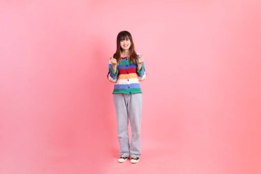 Renkli gökkuşağı kıyafetleri giyen Asyalı bir kadın ya da kalp şeklinde bir jest, küçük bir kalp, pembe arka planda izole edilmiş bir aşk. Gen Z