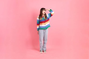 Renkli gökkuşağı kıyafetleri giyen Asyalı bir kadın ya da pembe arka planda izole edilmiş mesafeye bakma hareketi yapan sıradan bir görünüm. Gen Z