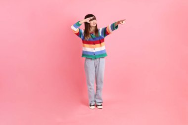 Renkli gökkuşağı kıyafetleri giyen Asyalı bir kadın ya da pembe arka planda izole edilmiş mesafeye bakma hareketi yapan sıradan bir görünüm. Gen Z