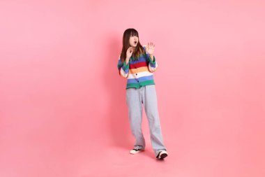 Renkli gökkuşağı kış kıyafetleri giyen Asyalı kadın ya da pembe arka planda izole edilmiş korku jestli sıradan bir görünüm. Gen Z