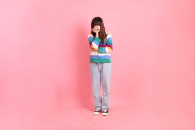 Renkli gökkuşağı kış kıyafetleri giyen Asyalı bir kadın ya da pembe arka planda izole edilmiş stres jesti içeren sıradan görünüşlü bir kadın. Gen Z