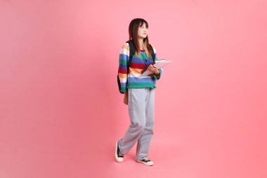 Renkli gökkuşağı kıyafetleri giyen Asyalı bir kadın ya da okul çantası ve kitap taşırken gelişigüzel giyinen pembe arka planda duran ve gülümseyen bir kadın. Gen Z